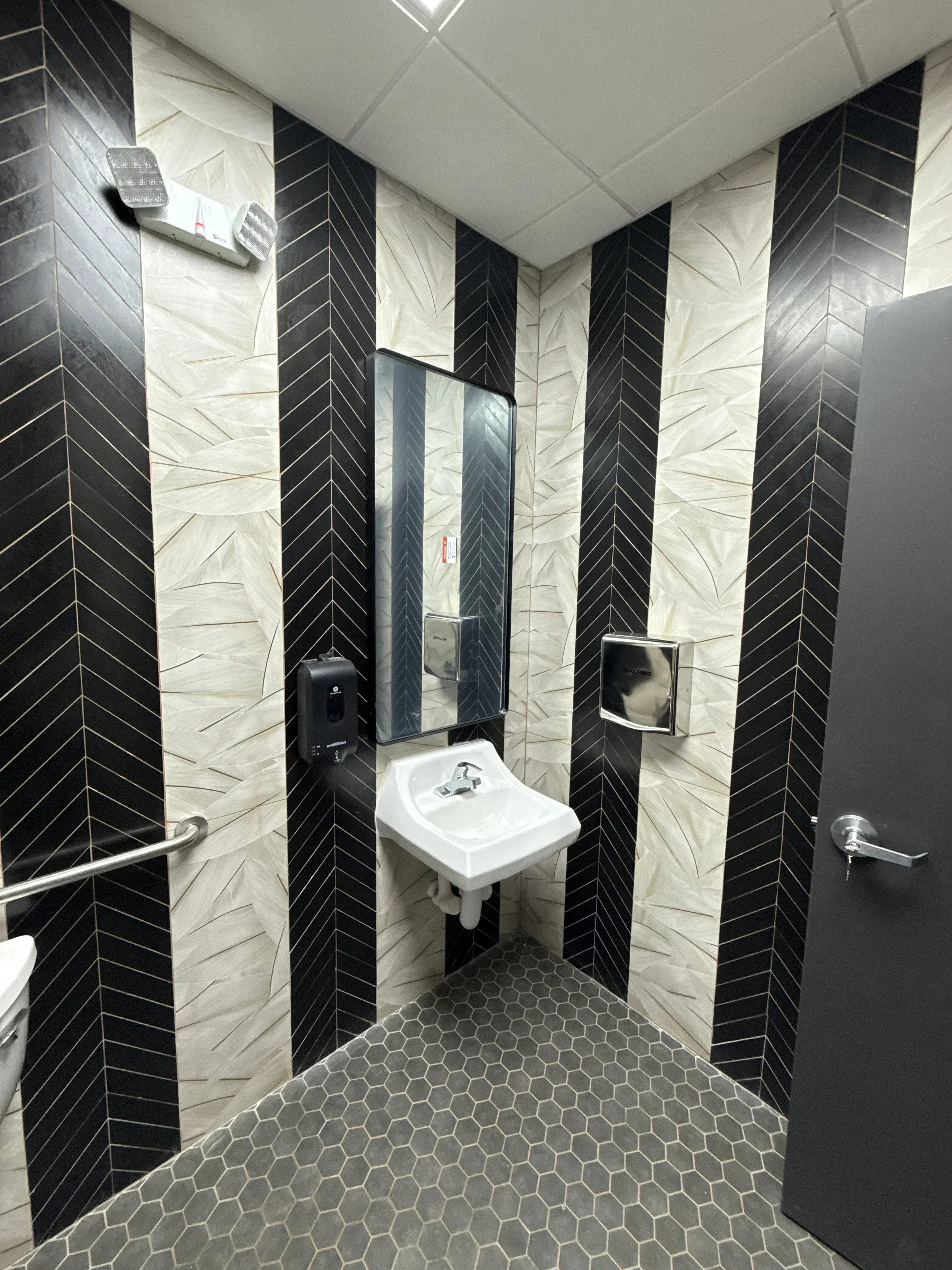 Black and white herringbone tile floor with hexagonal wall tiles and white pedestal sink