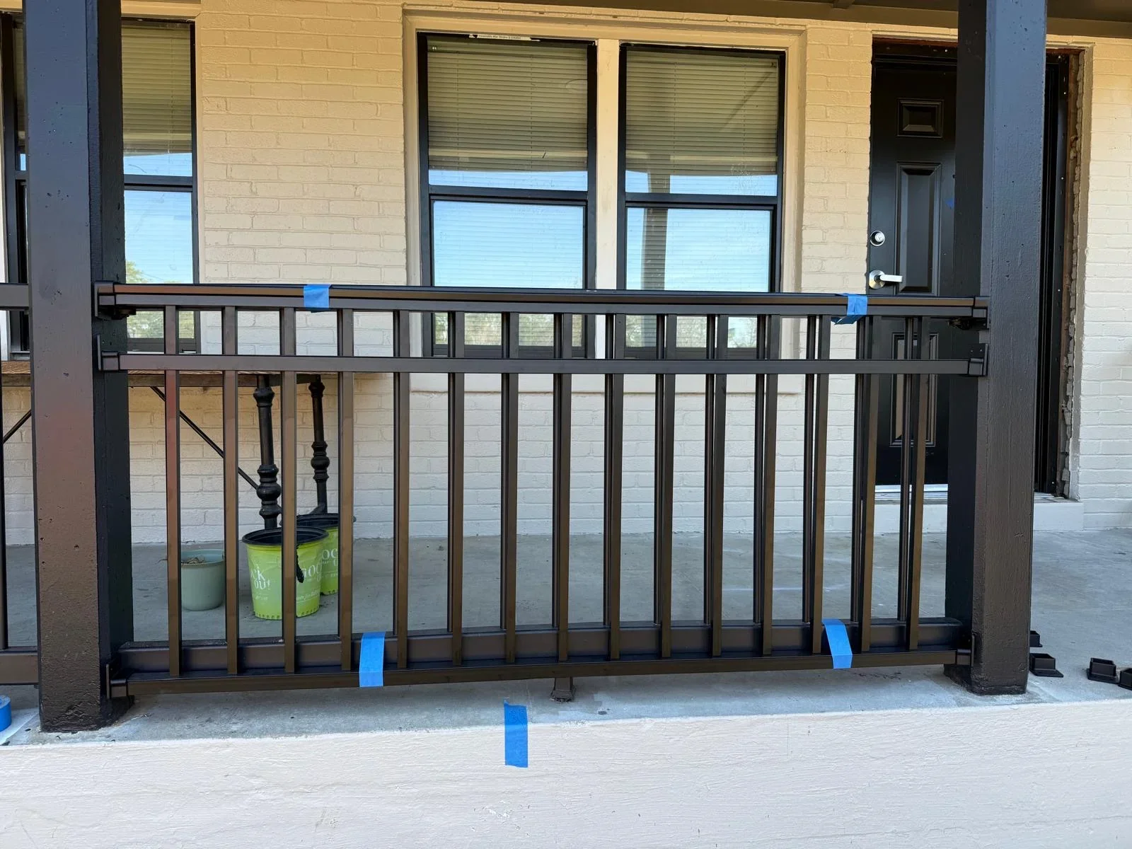 Black metal railing with vertical pickets and turned balusters on concrete patio