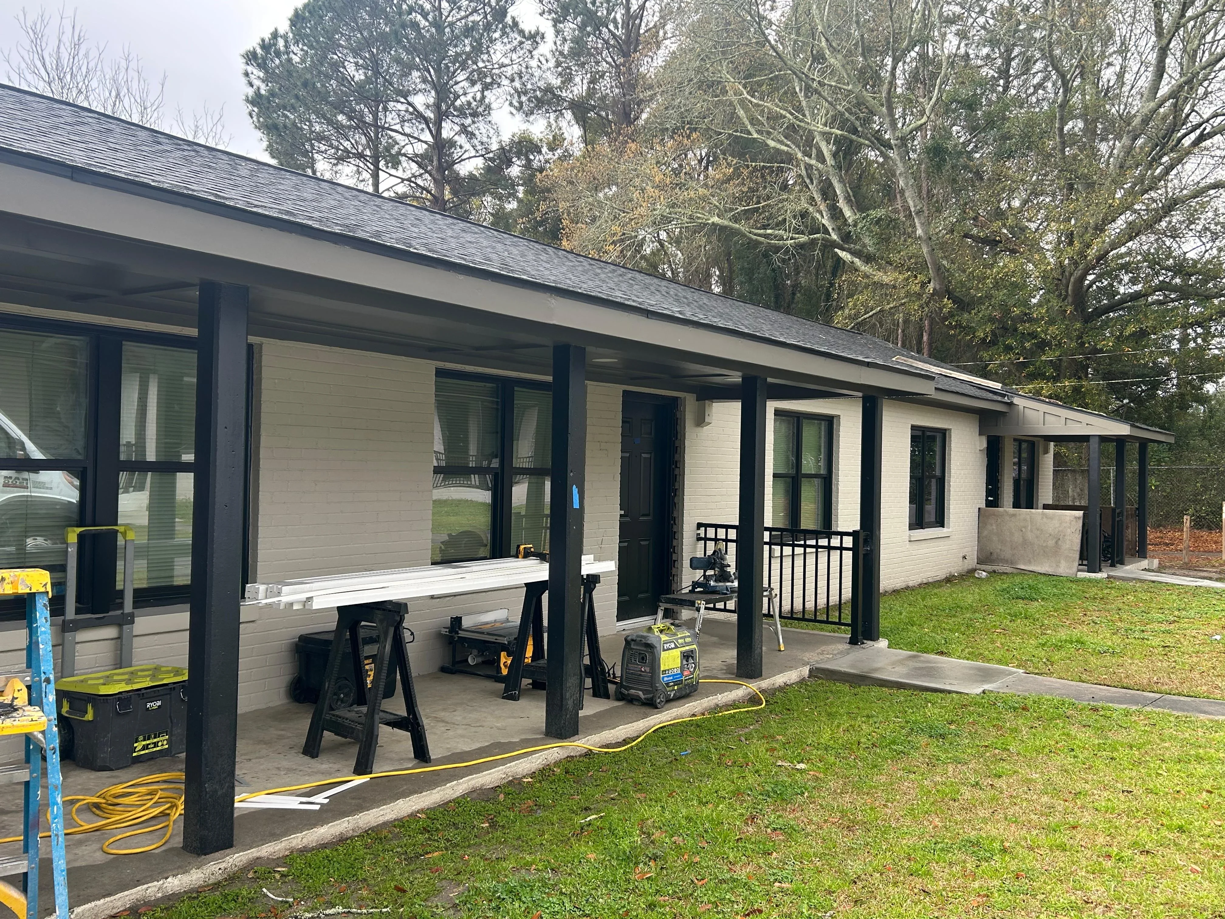 White brick home addition with black framing, large windows, and covered concrete patio