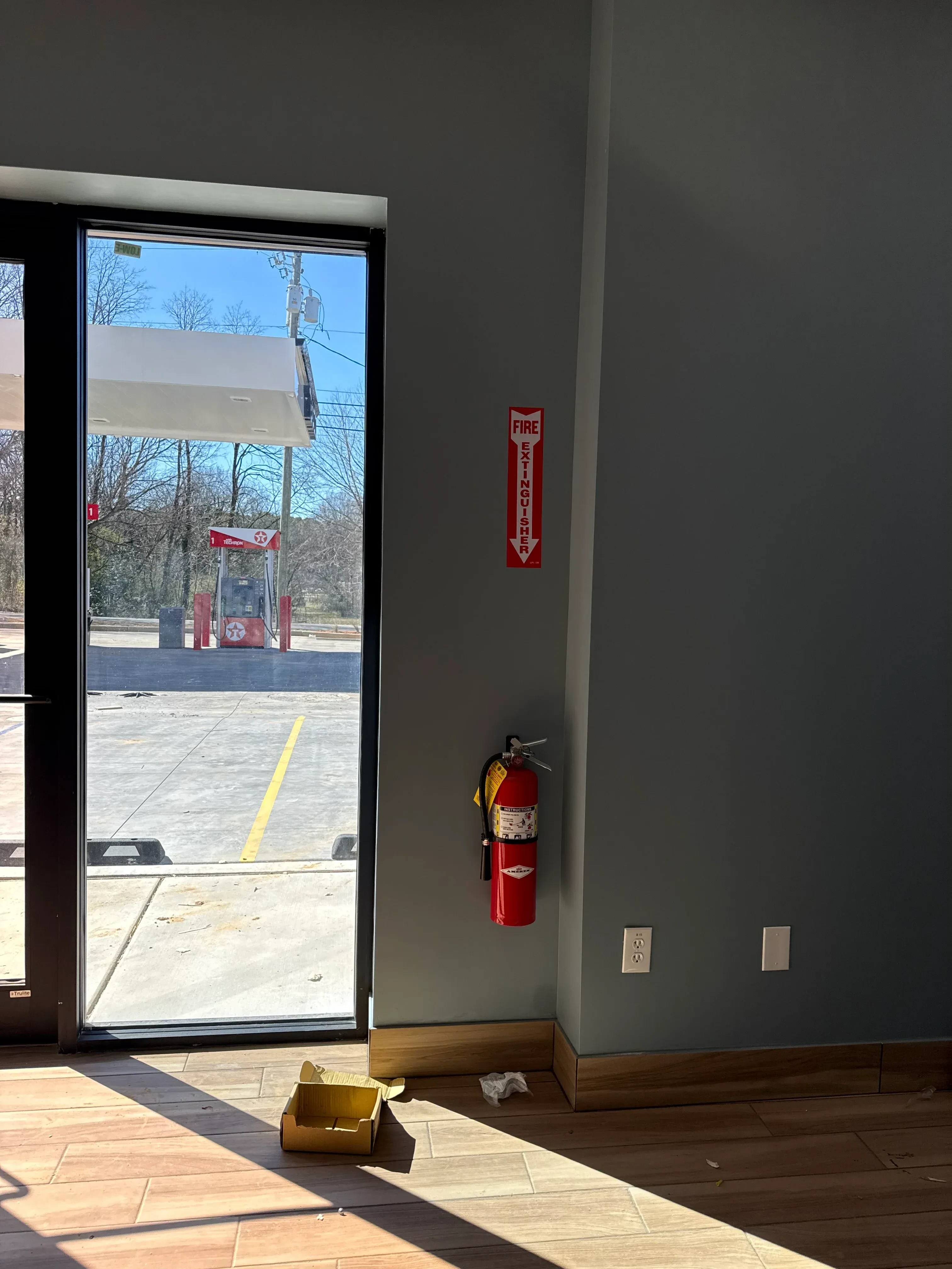 Gray drywall interior with electrical outlets, fire extinguisher, and large storefront window