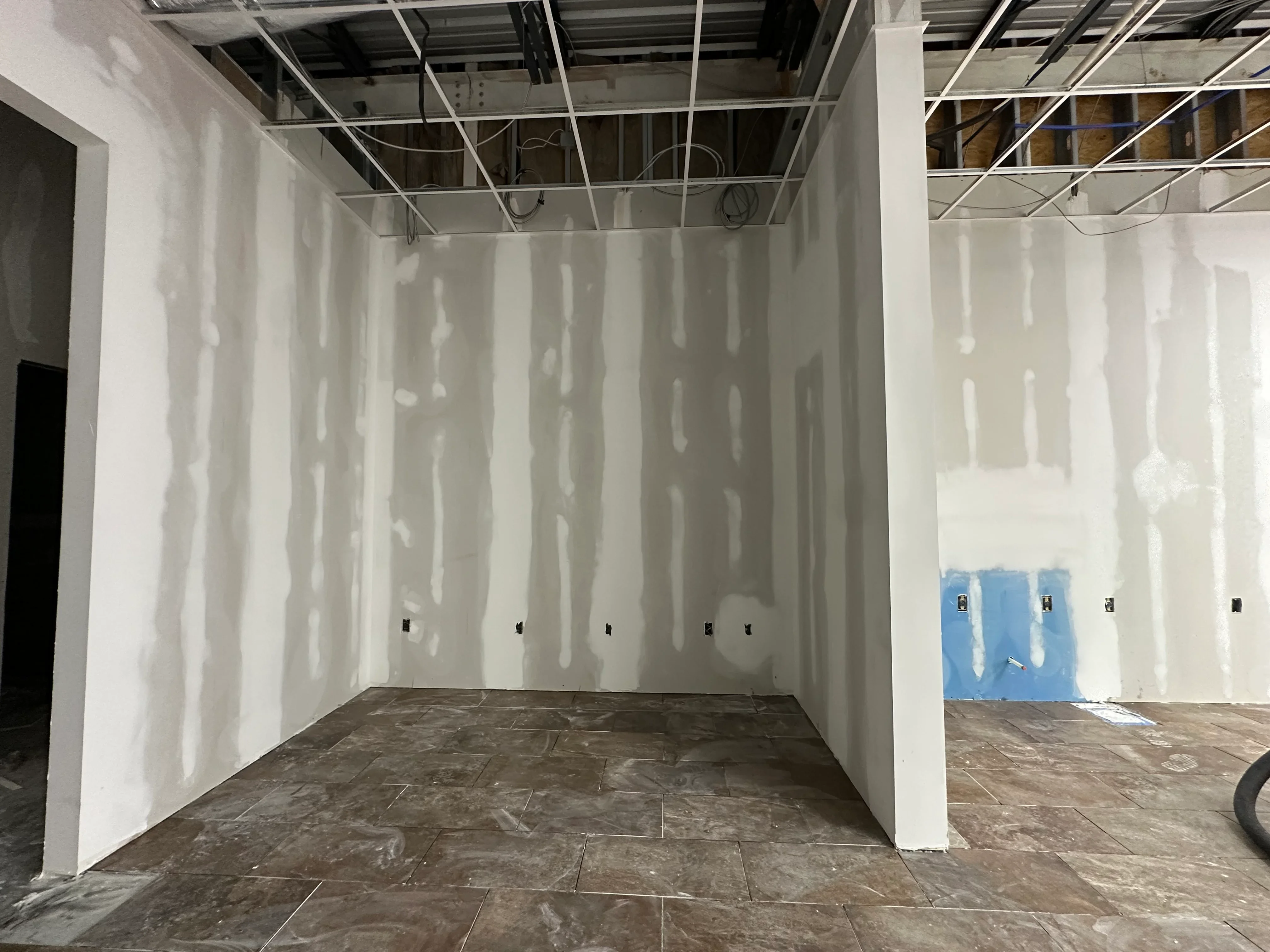Drywall interior with metal framing, suspended ceiling grid, and concrete flooring in commercial space