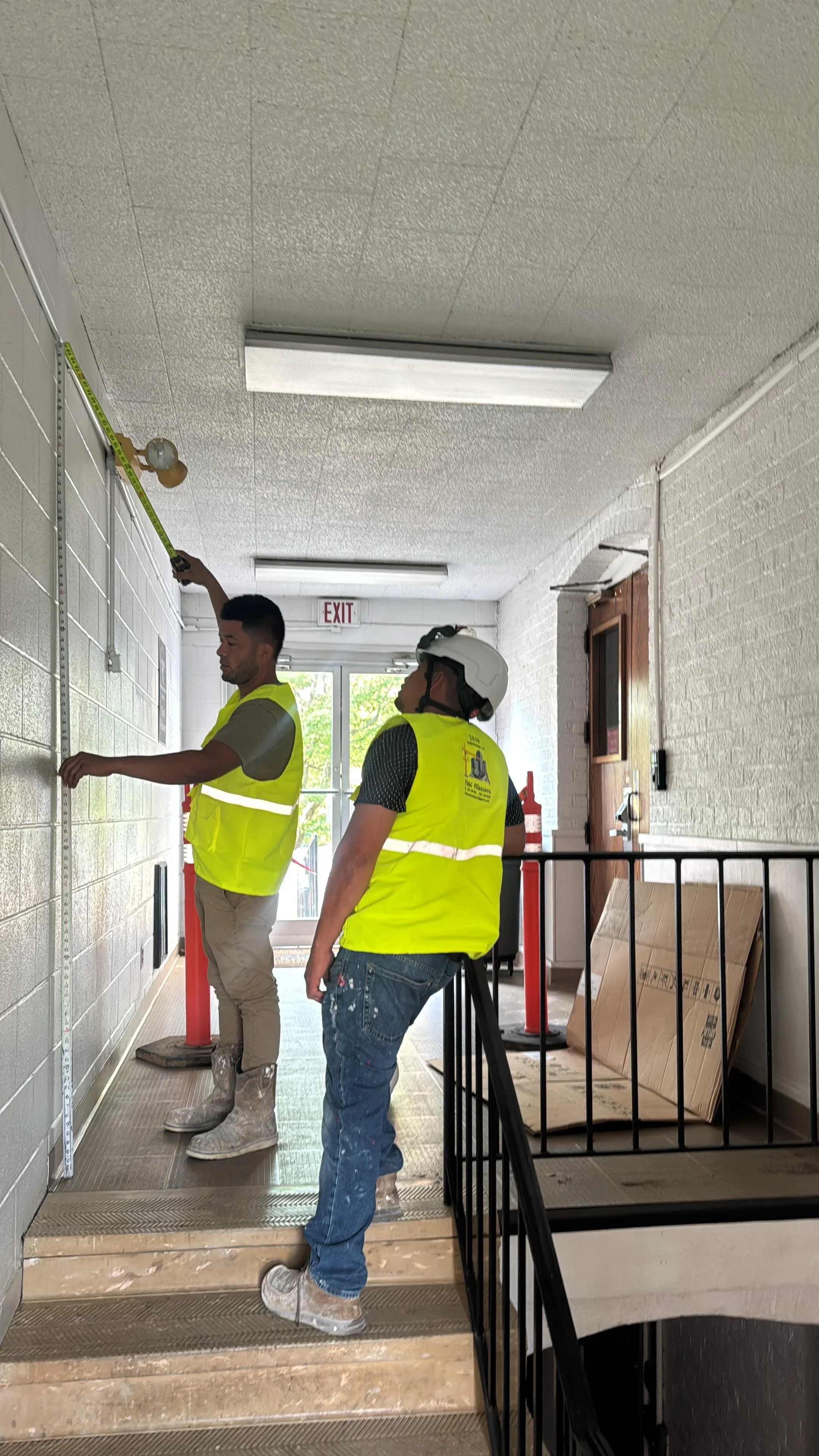 Workers installing white subway tile on hallway wall with textured ceiling and LED lighting