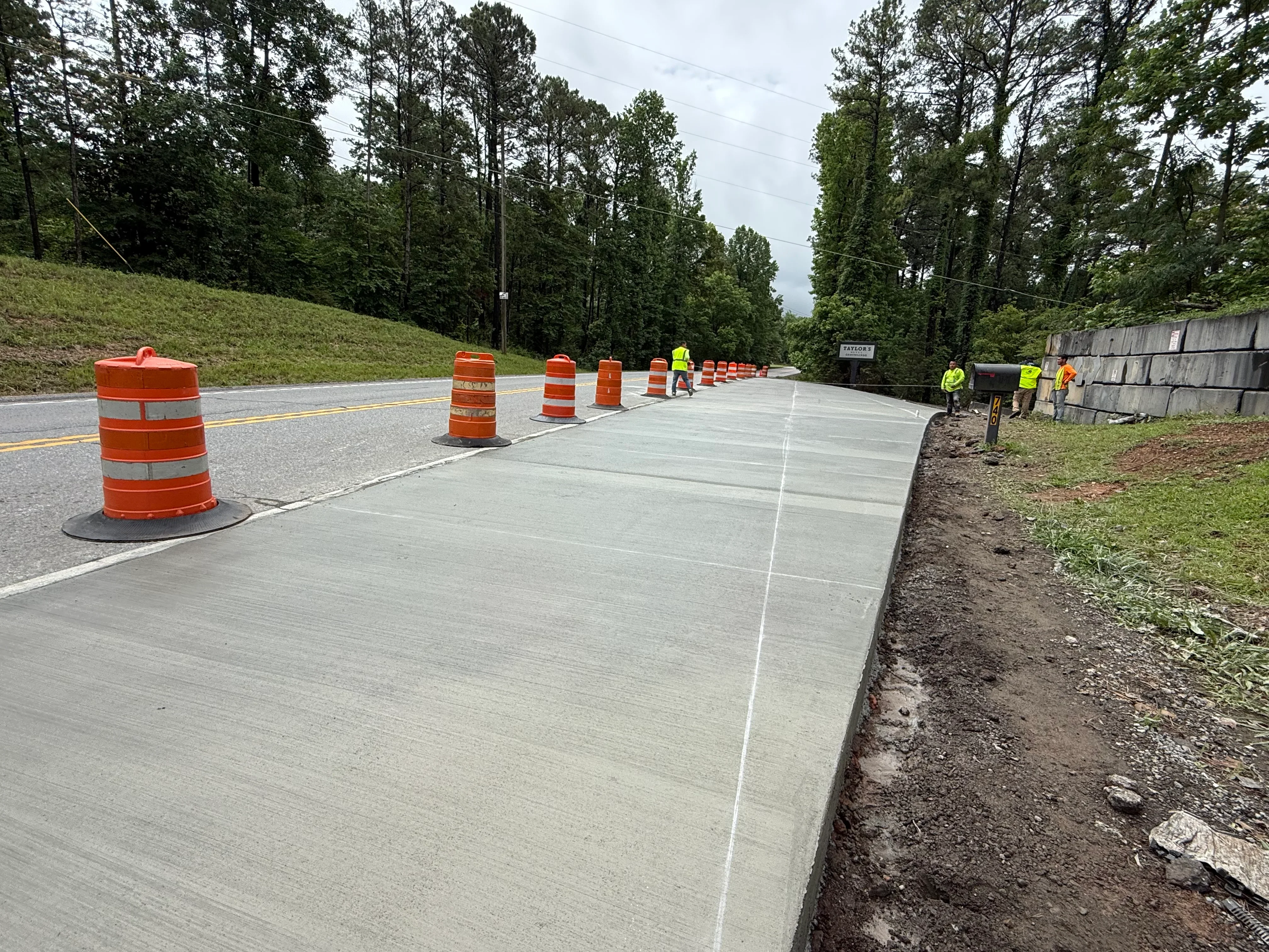 Newly poured concrete road with control joints, orange traffic barrels, and active site grading work