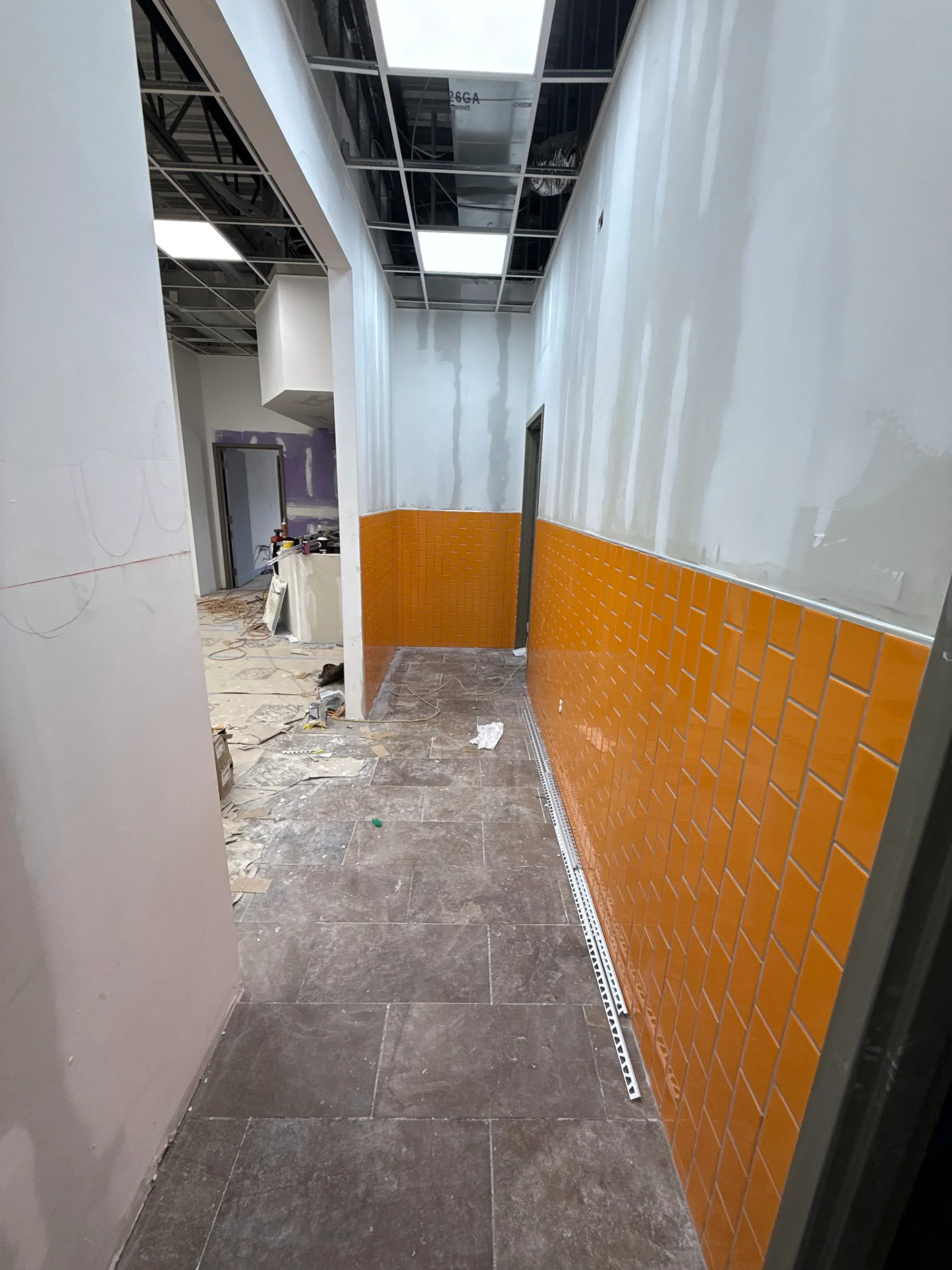 Commercial interior with orange acoustic ceiling tiles, gray tile walls, white drywall, and metal framing