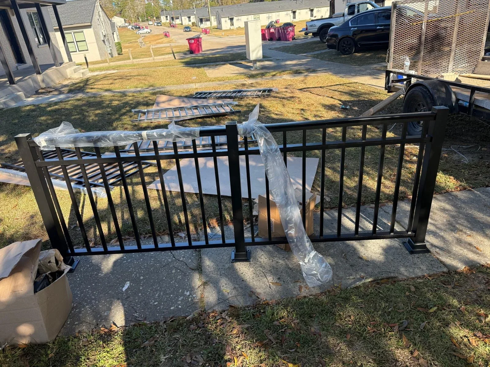 Black aluminum railing with vertical pickets installed on concrete, protective plastic wrapping visible