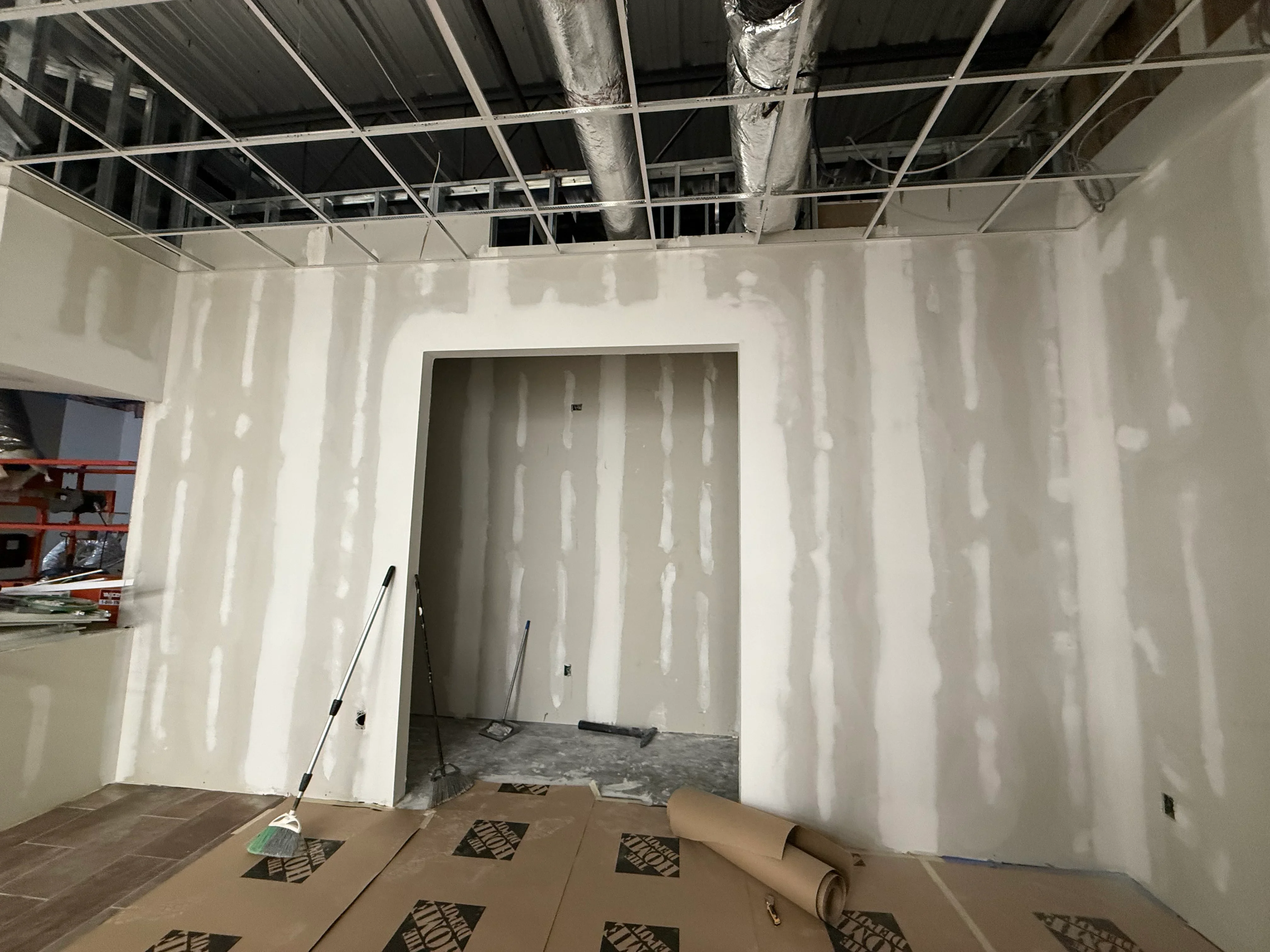 Drywall-taped walls with joint compound, metal stud framing, and suspended ceiling grid in commercial space