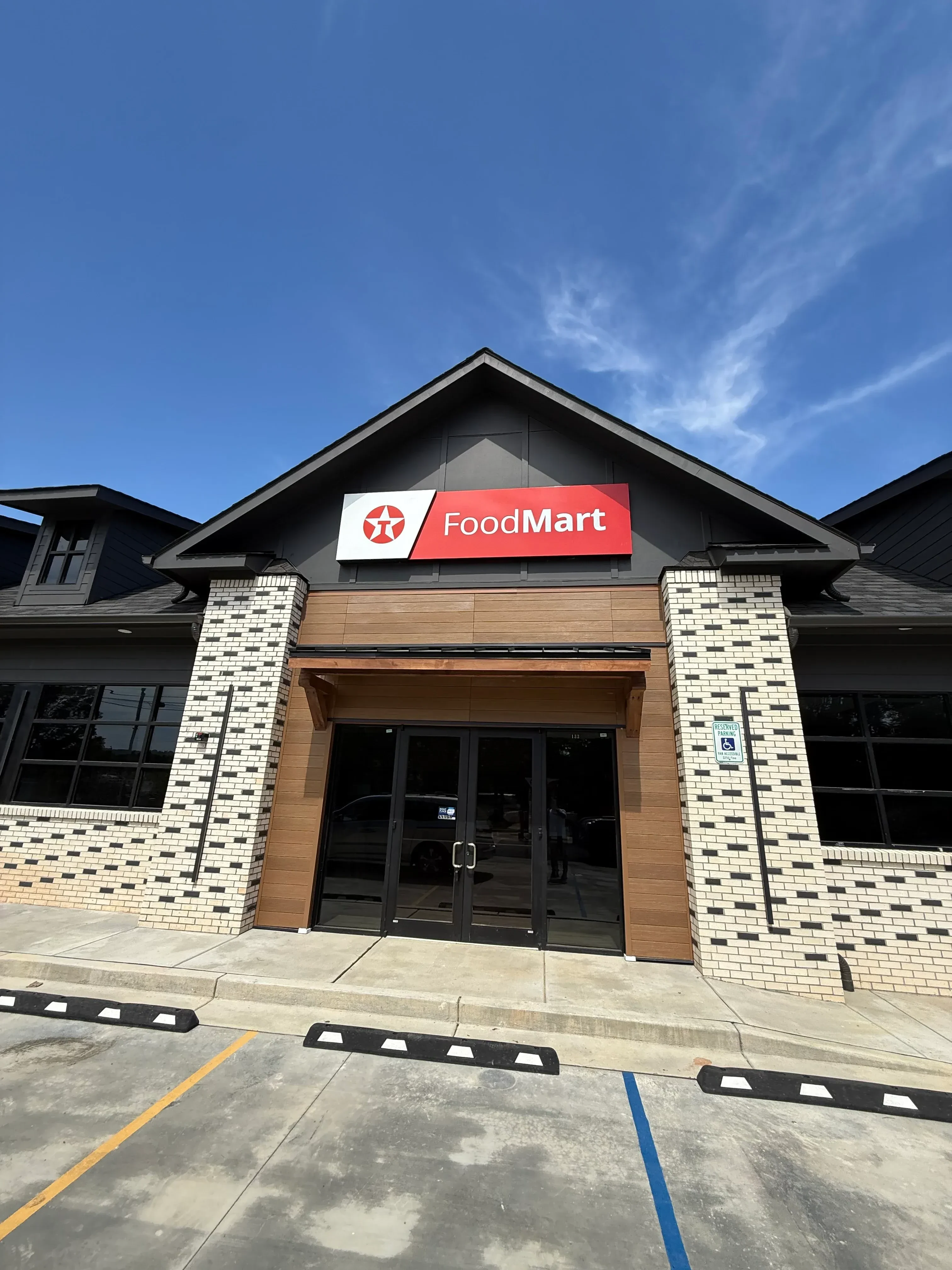 Commercial storefront with white geometric tile facade, wood cladding, and black aluminum framed entrance doors