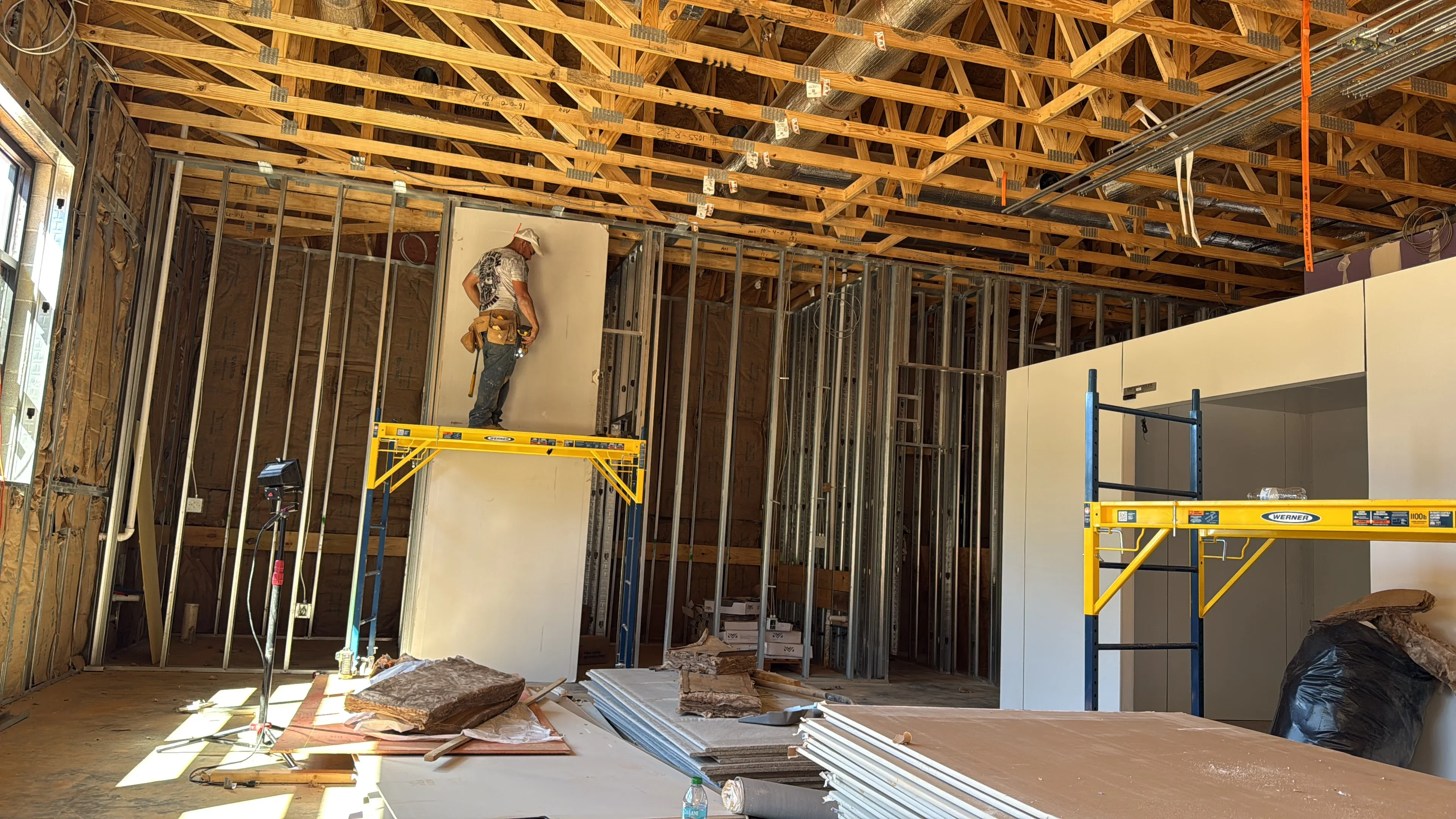 Metal stud framing with drywall installation, wooden roof trusses, and construction scaffolding
