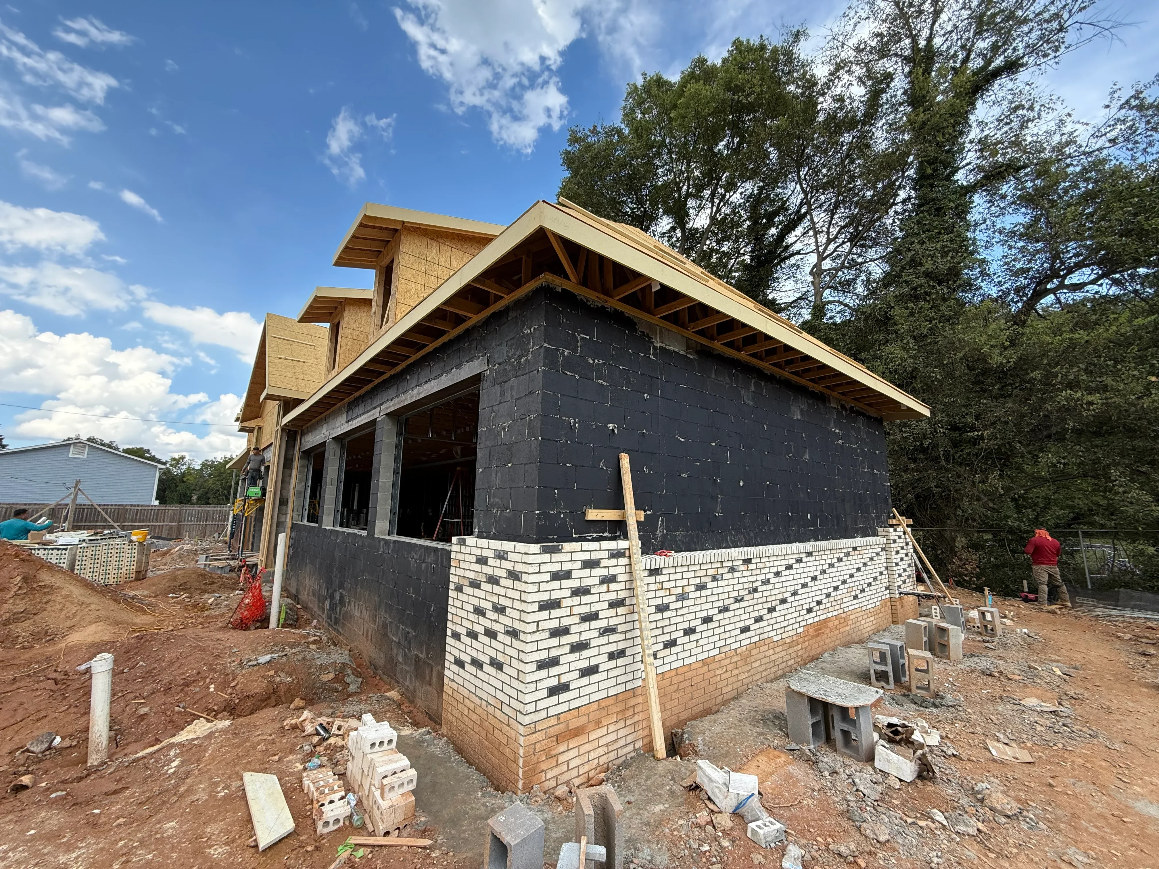 Residential home under construction with brick veneer, black weather wrap, and wooden roof framing