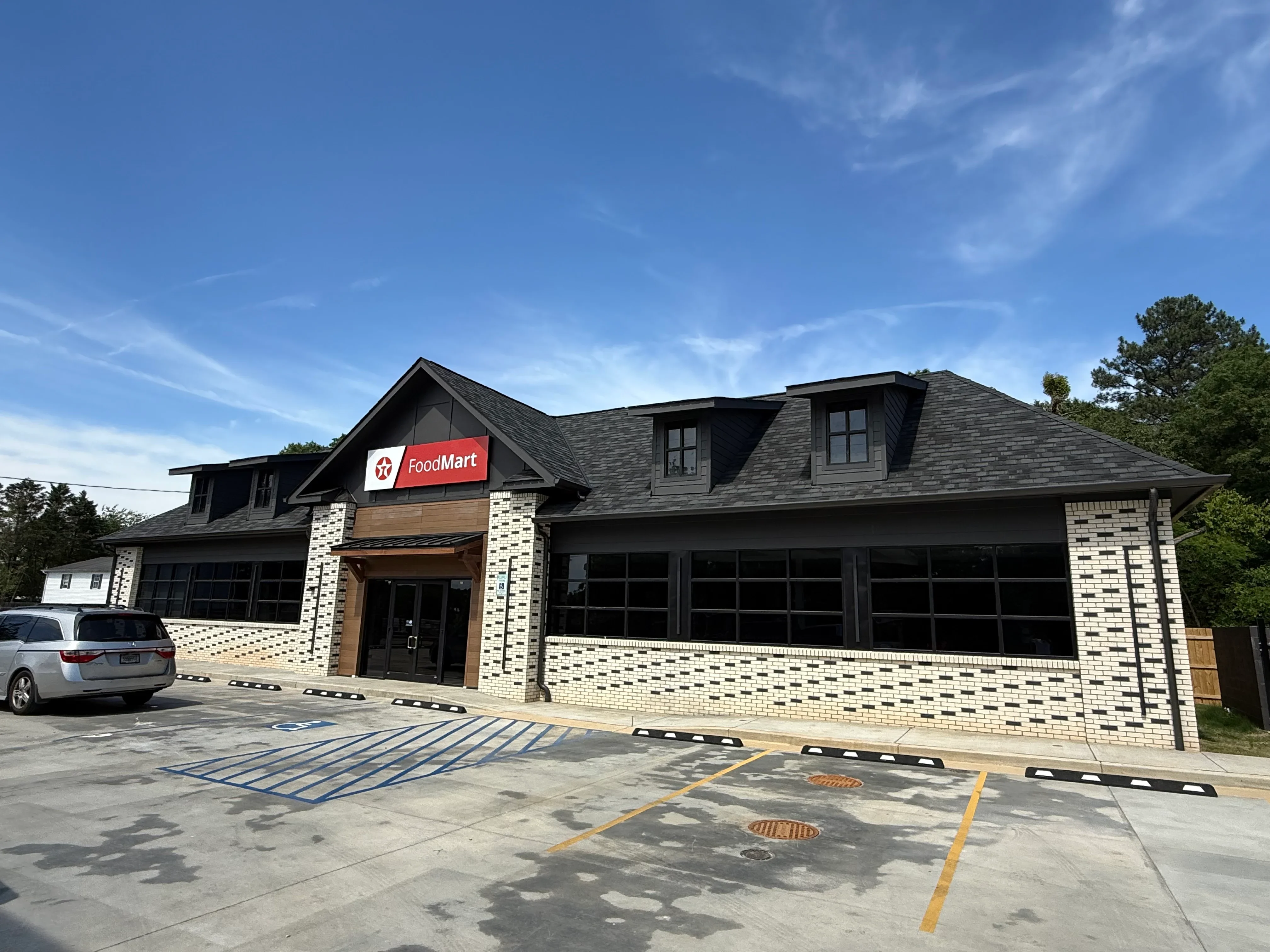 Cream brick commercial building with black roof, large storefront windows, and parking lot