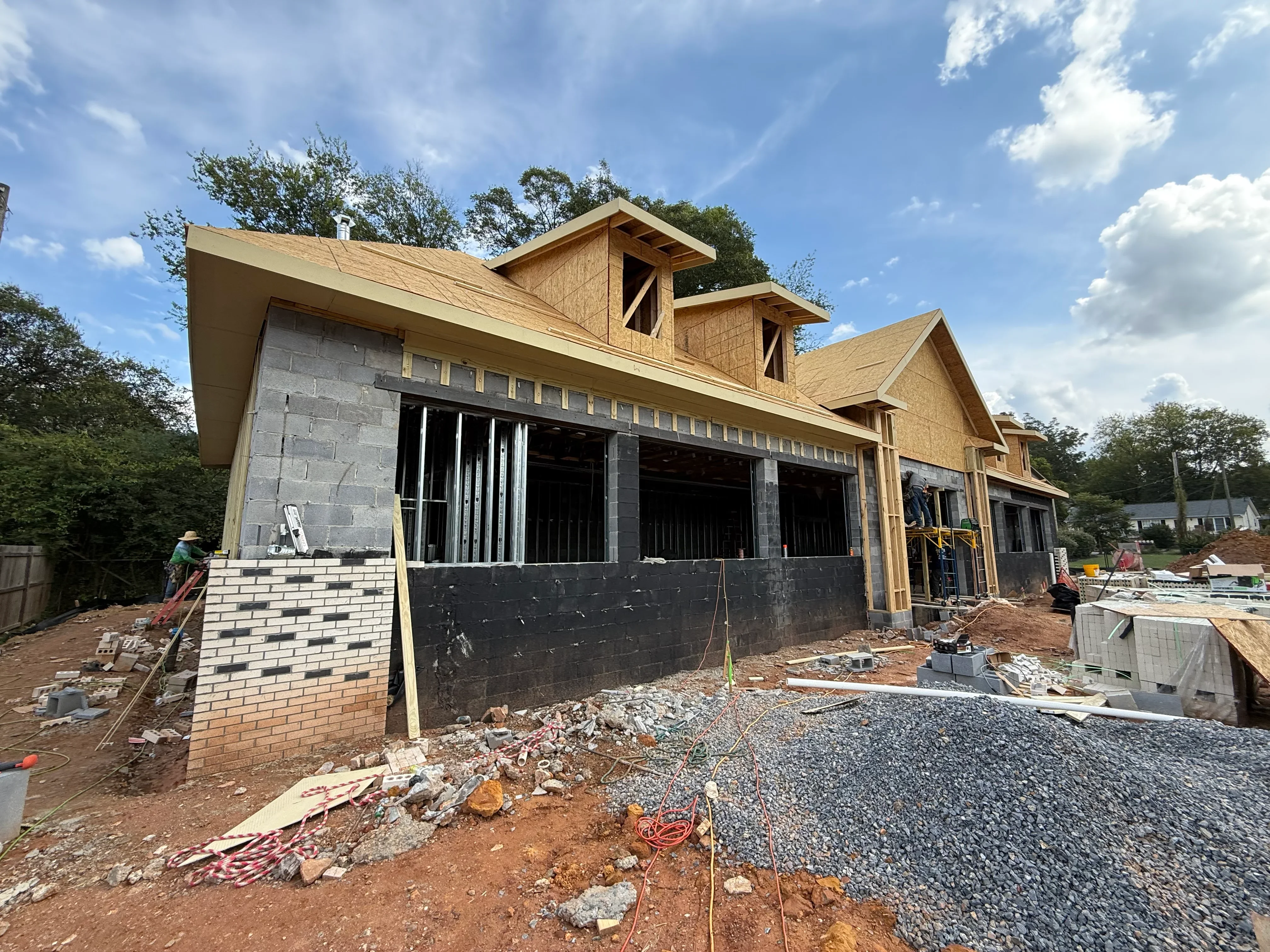 New home construction with brick foundation, wood framing, and shingle roof installation in progress
