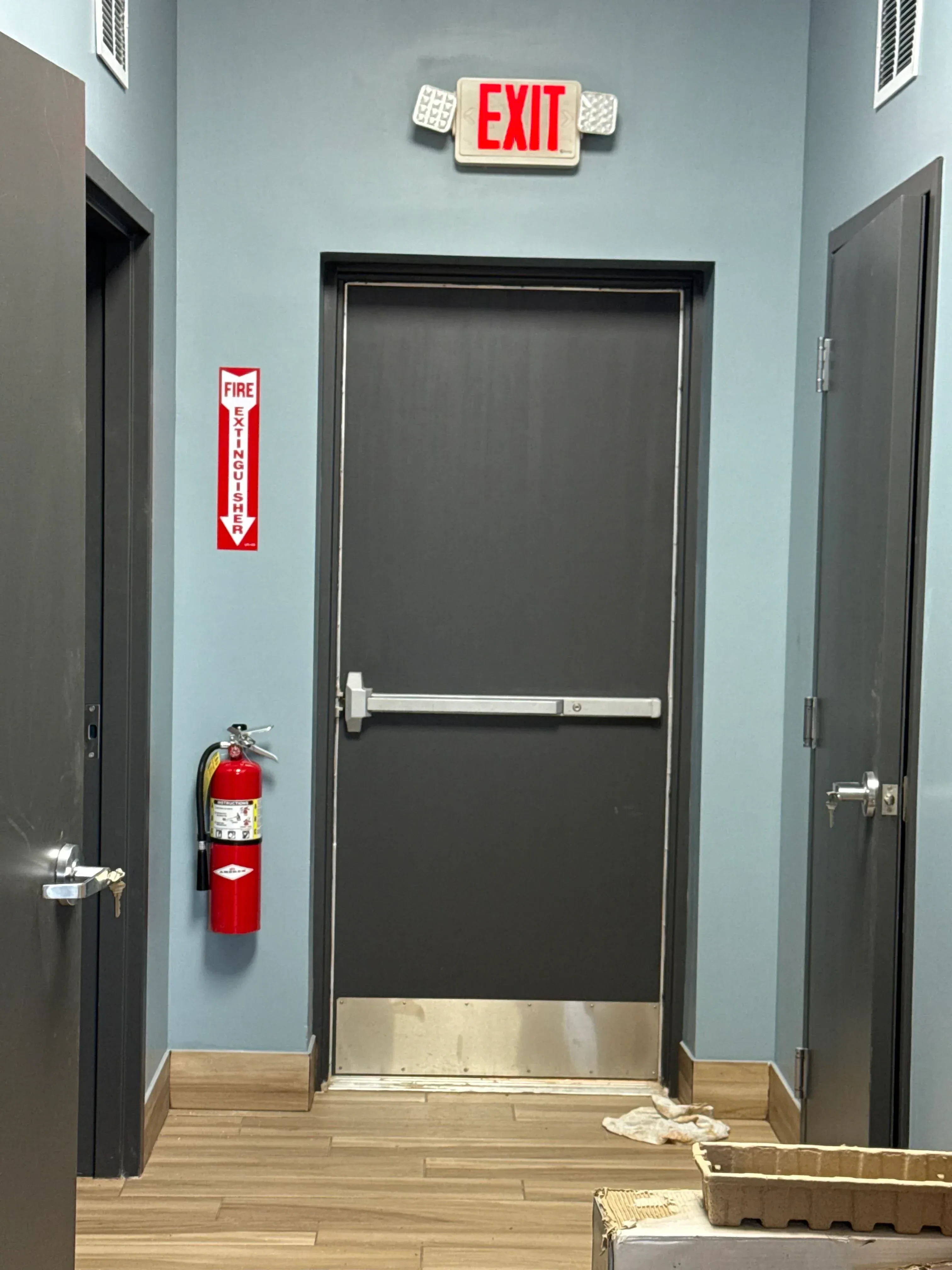 Black aluminum commercial exit door with panic bar hardware installed in blue painted wall