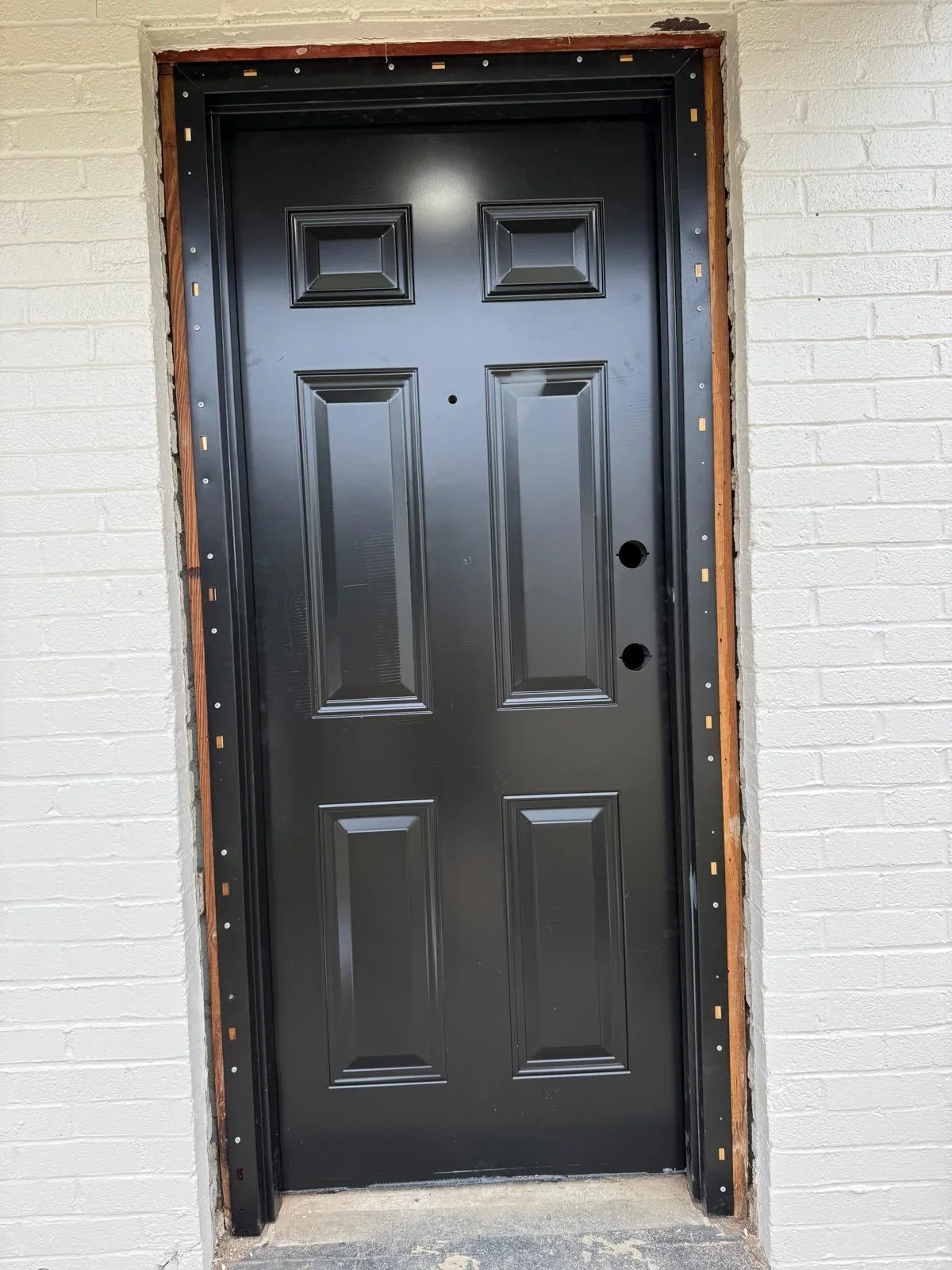 Black six-panel steel entry door with frame installation and white brick surround